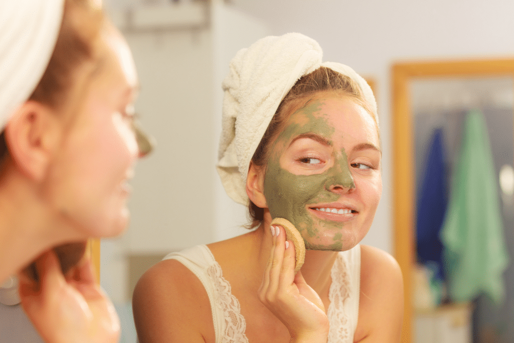 girl applying exfoliate mask to her half-face in the mirror