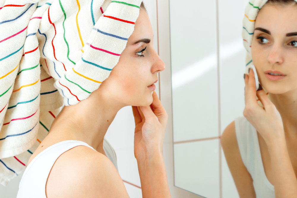 Face-washing girl, covering her head with a towel while she looks into the mirror