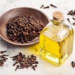 clove oil in a bottle and some clove in a plate and some on table